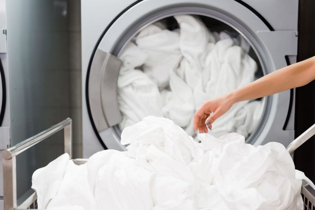 Hand entnimmt frisch gewaschene Hotelwäsche aus einer Industriewaschmaschine