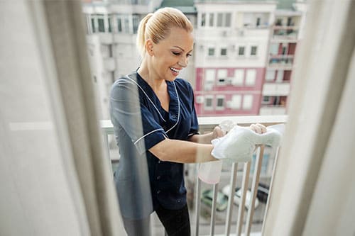 Hotelmitarbeiterin reinigt Fenster auf dem Balkon – professionelle Fensterreinigung durch Glanz & Glorie Hotel Service