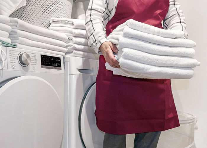 Glanz & Glorie Hotel Service – effiziente Wäschereiarbeit mit gefalteten Handtüchern vor modernen Waschmaschinen